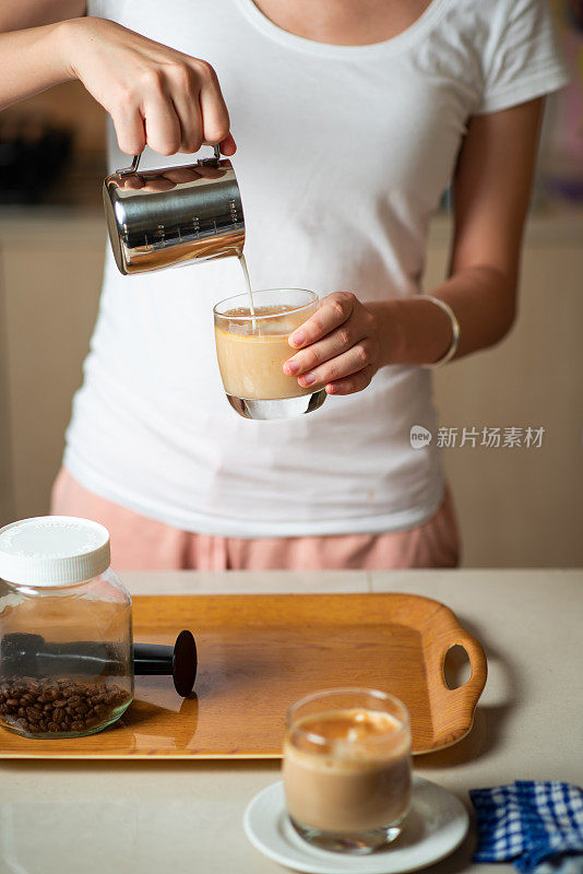 Woman pouring frothed milk into espresso while making a latte cappuccino coffee